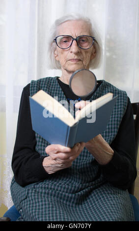 Ninety years old grandma reading a book through magnifying glass Stock Photo