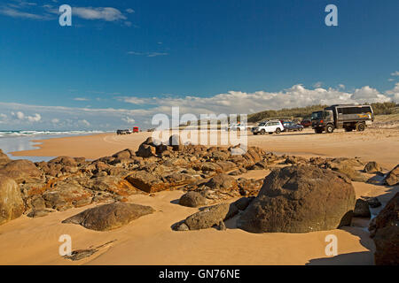 Vast sandy 75-mile beach, ocean & rocks near Indian Head on Fraser Island with vehicles on unusual highway under blue sky Stock Photo