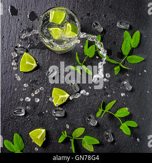 beautiful mojito cocktail with splash, ice, green mint, limes and drops on black slate stone background, close up Stock Photo