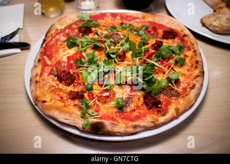 Meat feast pizza with pepperoni and ground beef topped with rocket served in restaurant Stock Photo