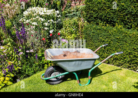 Old well used rusty wheelbarrow in a summer garden. Stock Photo