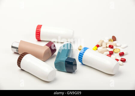 Different types of asthma inhalers laying next to some loose pills on a white background Stock Photo