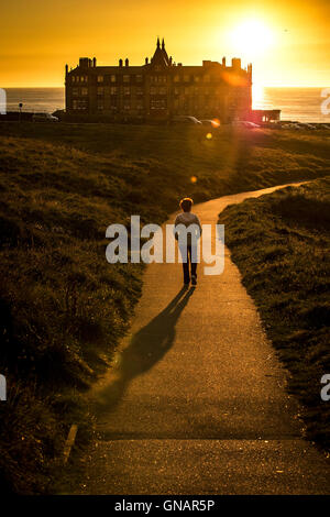 A woman walks along a path during an intense sunset over the Headland in Newquay, Cornwall.