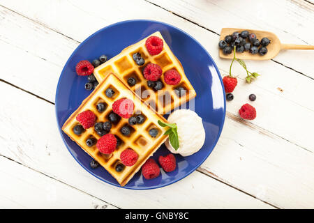Belgian waffles with raspberries, blueberries and vanilla ice cream scoop on blue plate, on rustic wooden table Stock Photo