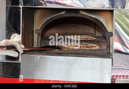 man putting freshly made pizza in a wood fired pizza oven Stock Photo