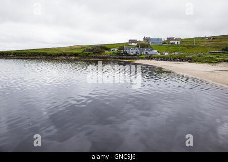 Sandy beach in MId Yell on the Shetland Islands with a few houses and calm sea Stock Photo