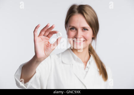 Doctor woman showing pill. Young female medical professional isolated on white background. Selective focus. Stock Photo