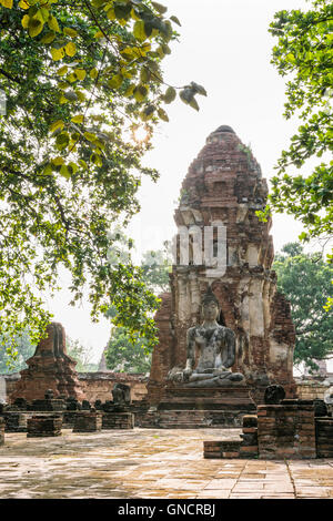 Buddha statue sitting position at front of pagoda under sun light surround by trees and ancient ruins of Wat Phra Mahathat templ Stock Photo