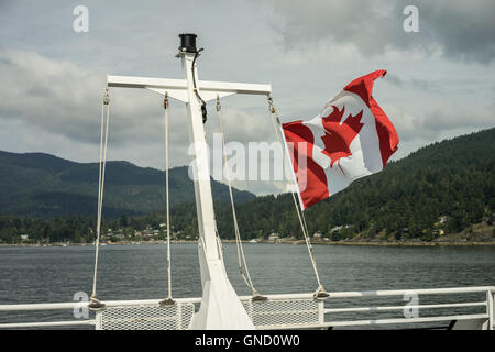 The Canadian flag flaps in the wind at the rear of a B.C. ferry leaving Snug Cove on Bowen Island near Vancouver, British Columb Stock Photo