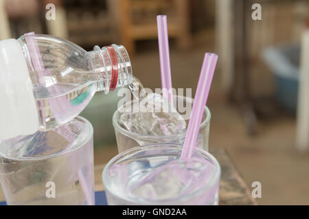 Water pouring on a plain glass with ice and pink straw. Selective focus. Stock Photo