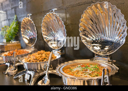 Buffet line food containers shaped shells, with dark bricks wall background. Selective focus. Stock Photo