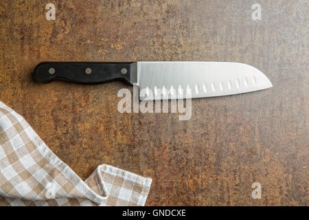 The kitchen knife and checkered napkin on old rusty background. Top view. Stock Photo
