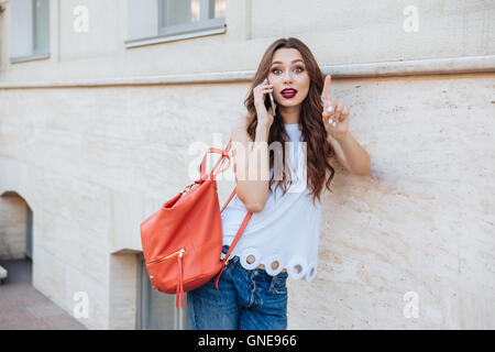 Young beautiful brunette girl talking on the phone and leaning on the wall outdoors Stock Photo