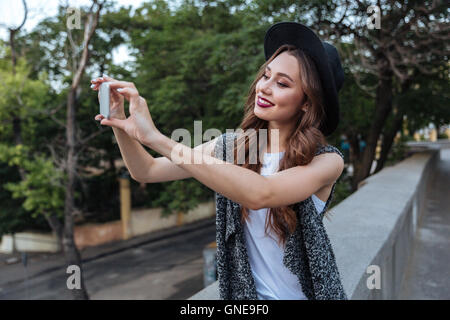 Young beautiful stylish brunette girl making selfie with her phone outdoors Stock Photo