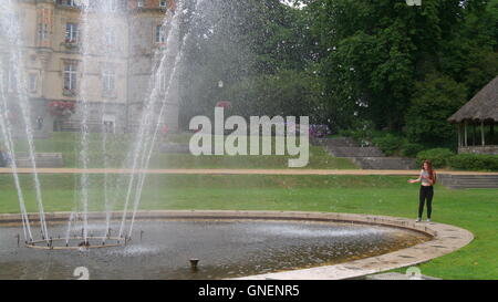 A little wet girl is cooling off in a fountain on a hot summer day ...