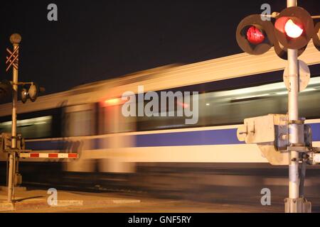 Train Passes Railroad Crossing. A train passing in speed through a level crossing at night. Railway crossing (railroad crossing) with speeding passeng Stock Photo