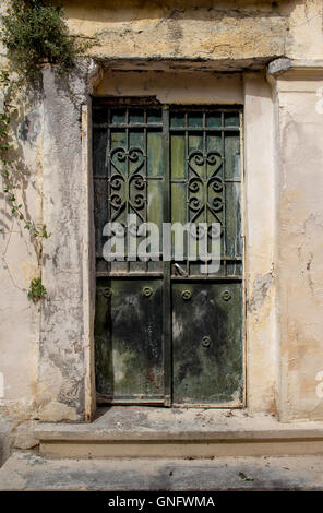 Facade of an old house. Entrance green iron door with a heart design grid. Plant in the corner on the wall. Athens in Greece.