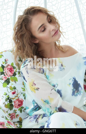 Beautiful woman with closed eyes, smiling. He is sitting in a chair. Bright interior. Flowers. Stock Photo