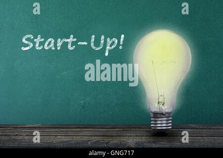 Start-up text on green board and light bulb on table Stock Photo