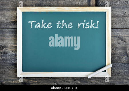 Take the risk text on school board and chalk on wooden table Stock Photo