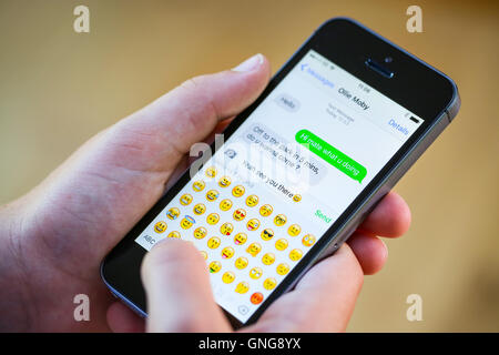 A teenage boy using an emoji whilst texting on his iphone Stock Photo