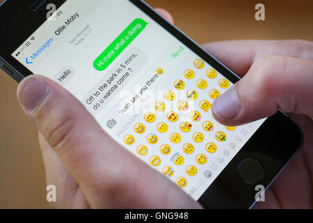 A teenage boy using an emoji whilst texting on his iphone Stock Photo