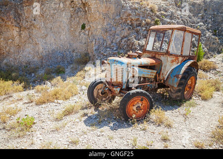 Old abandoned rusted tractor stands on dry summer meadow in Greece Stock Photo