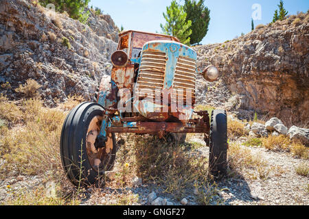 Old abandoned rusted tractor stands on dry summer grass, front view Stock Photo