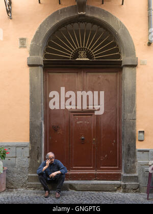 Senior man talking on mobile phone in front of doorway, Orvieto, Terni Province, Umbria, Italy Stock Photo
