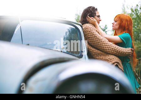 Bright trendy couple having fun and kissing outdoors near old vintage car. Boho style. Stock Photo