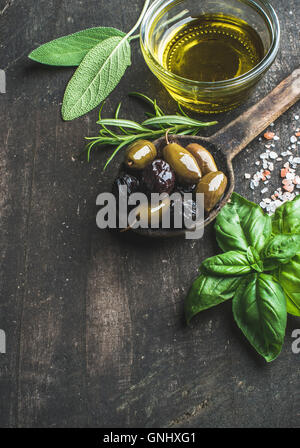 Green and black Mediterranean olives in old cooking spoon with olive oil and herbs over dark rustic wooden background, top view, Stock Photo