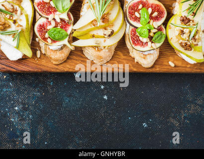 Crostini with pear, ricotta cheese, figs, nuts and fresh herbs. Breakfast toasts or snack sandwiches on rustic wooden board over Stock Photo