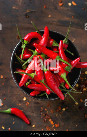 Black bowl of fresh red hot chili peppers and dry chilli flakes over old wooden textured background. Spicy theme. Top view Stock Photo