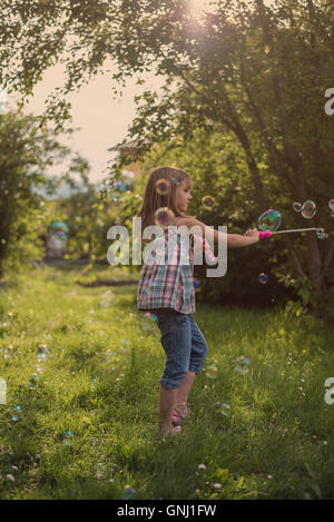 Girl blowing bubbles with bubble wand in garden Stock Photo