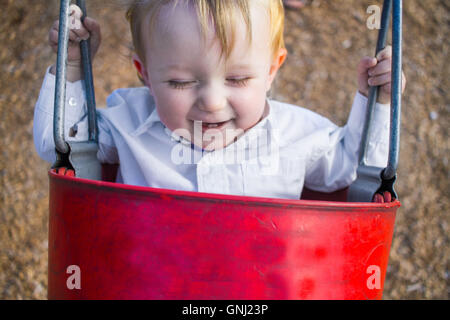 Smiling boy sitting in bucket swing Stock Photo