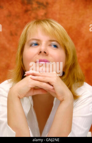 blond woman in her thirty with her hands under her chin, wearing a white shirt, glancing sideway Stock Photo