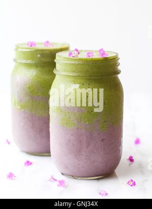 Two Green and Purple fruit and vegetable Smoothie drinks with flower decoration Stock Photo