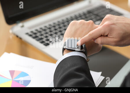 Businessman hands using a smart watch with the finger on the touch screen sitting in a desktop at office with a computer Stock Photo