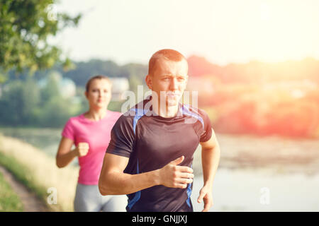 Young athletic people jogging outdoor near pond. Man and woman doing run workout in the park Stock Photo