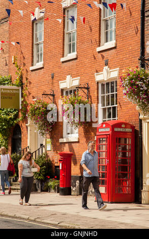 People walking past Red round post box and traditional red telephone box outside Ashbourne Heritage Center,Ashbourne ,Derbyshire Stock Photo