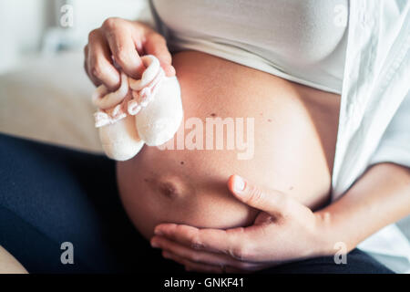 Pregnant woman shows her belly and the white woolen shoes of the future child. Stock Photo