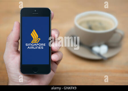 A man looks at his iPhone which displays the Singapore Airlines logo, while sat with a cup of coffee (Editorial use only). Stock Photo