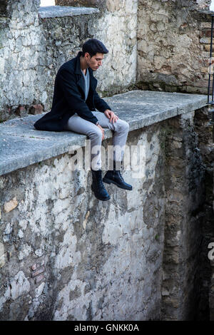 Portrait of good-looking man looking down while sitting on stone edge Stock Photo
