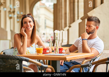 A handsome guy is upset to his beautiful girlfriend because she is talking on the phone while they are having a coffee at a tabl Stock Photo