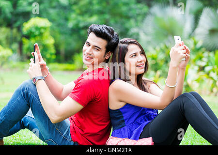 2 Young Girl and Boy Friends College Student Park Sitting Chatting Mobile phone Stock Photo