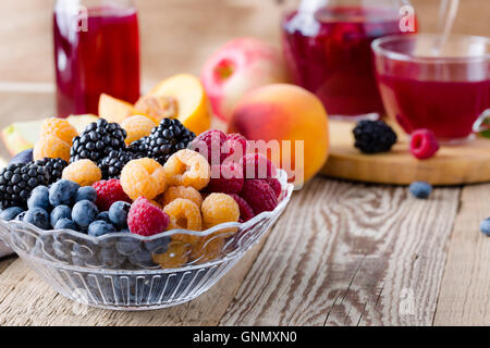 Fresh summer berries and fruits in  glass bowl and fruit tea with raspberries, blackberries and blueberries on wooden table Stock Photo