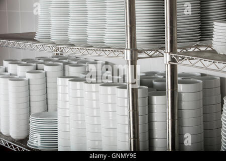 stacks of many white plates on a wire rack shelf in a commercial kitchen Stock Photo