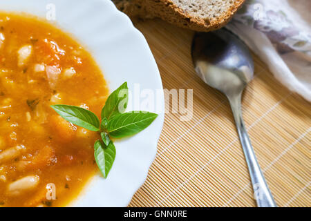 Cooked beans served in white plate with basil leaves and whole wheat bread on wooden background Stock Photo