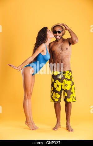 Pretty girl in swimsuit kissing her african boyfriend isolated on orange background Stock Photo