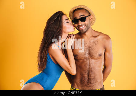 Pretty girl in swimsuit kissing her african boyfriend isolated on orange background Stock Photo